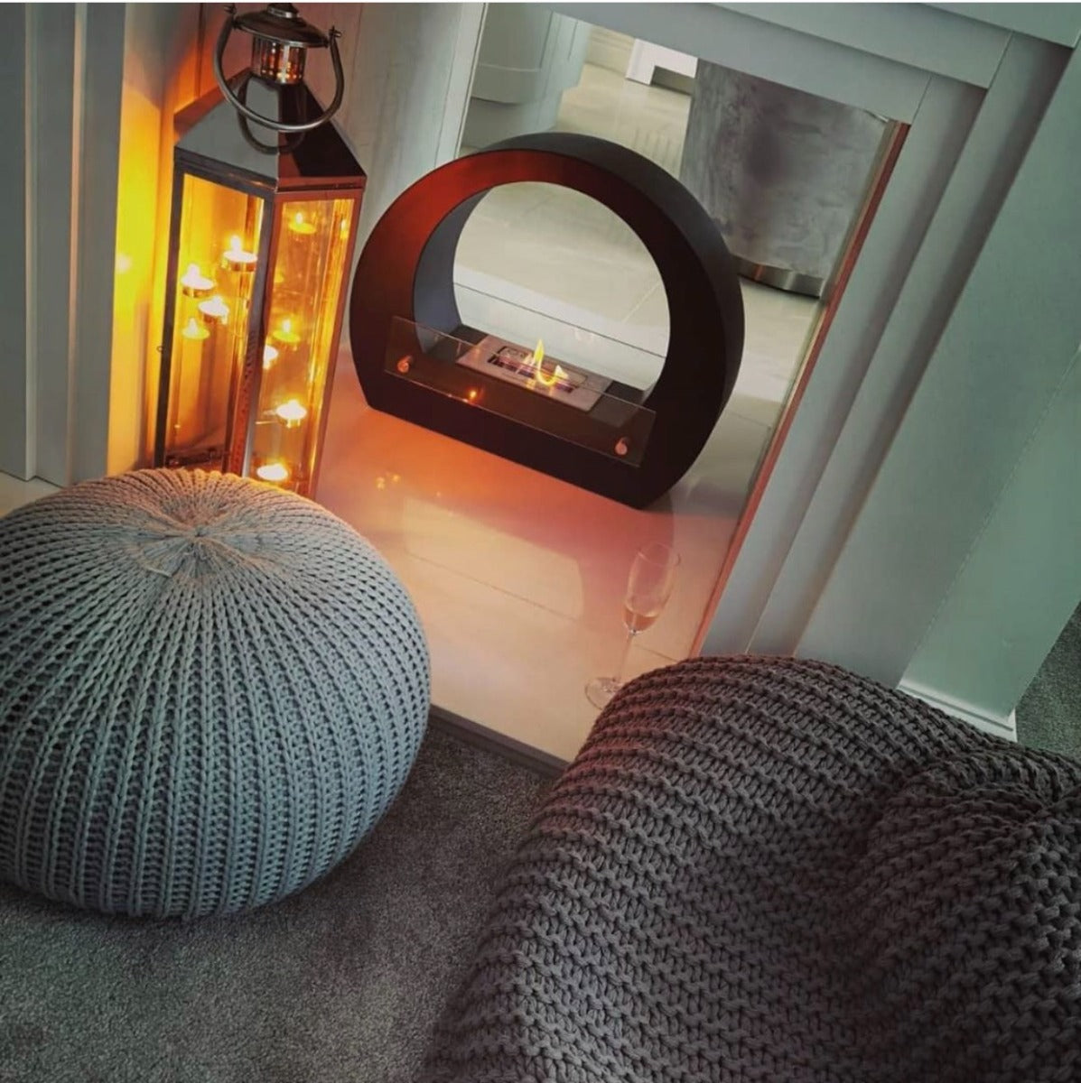 Round black bioethanol fireplace next to a lantern with tea lights inside and grey furniture