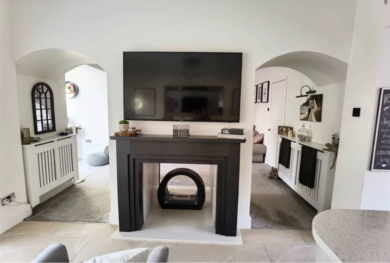 Round black bioethanol fireplace positioned in the centre of a living room under a large TV