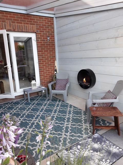 Round black bioethanol fireplace mounted on the wall outdoors next to grey chairs