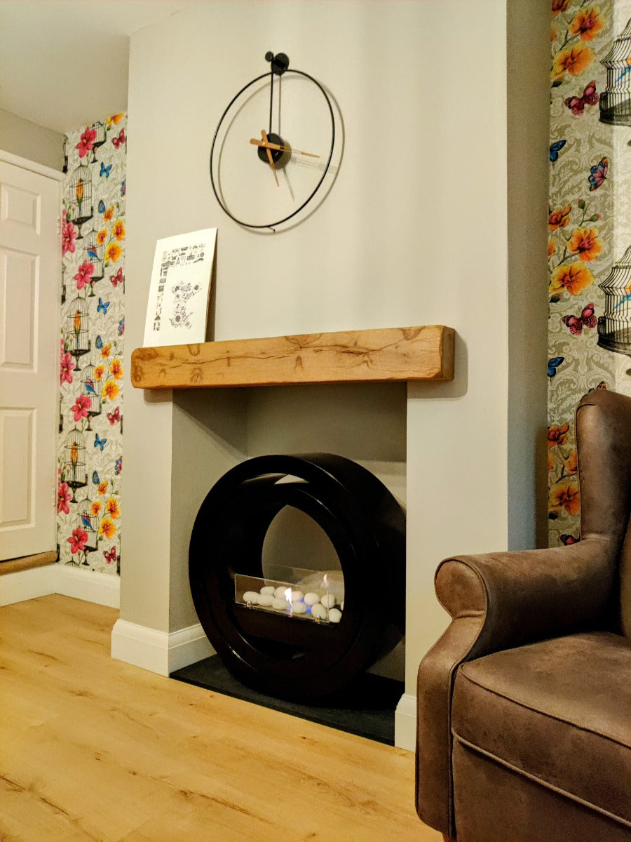 Round black bioethanol fireplace in a beige insert with a contemporary clock above