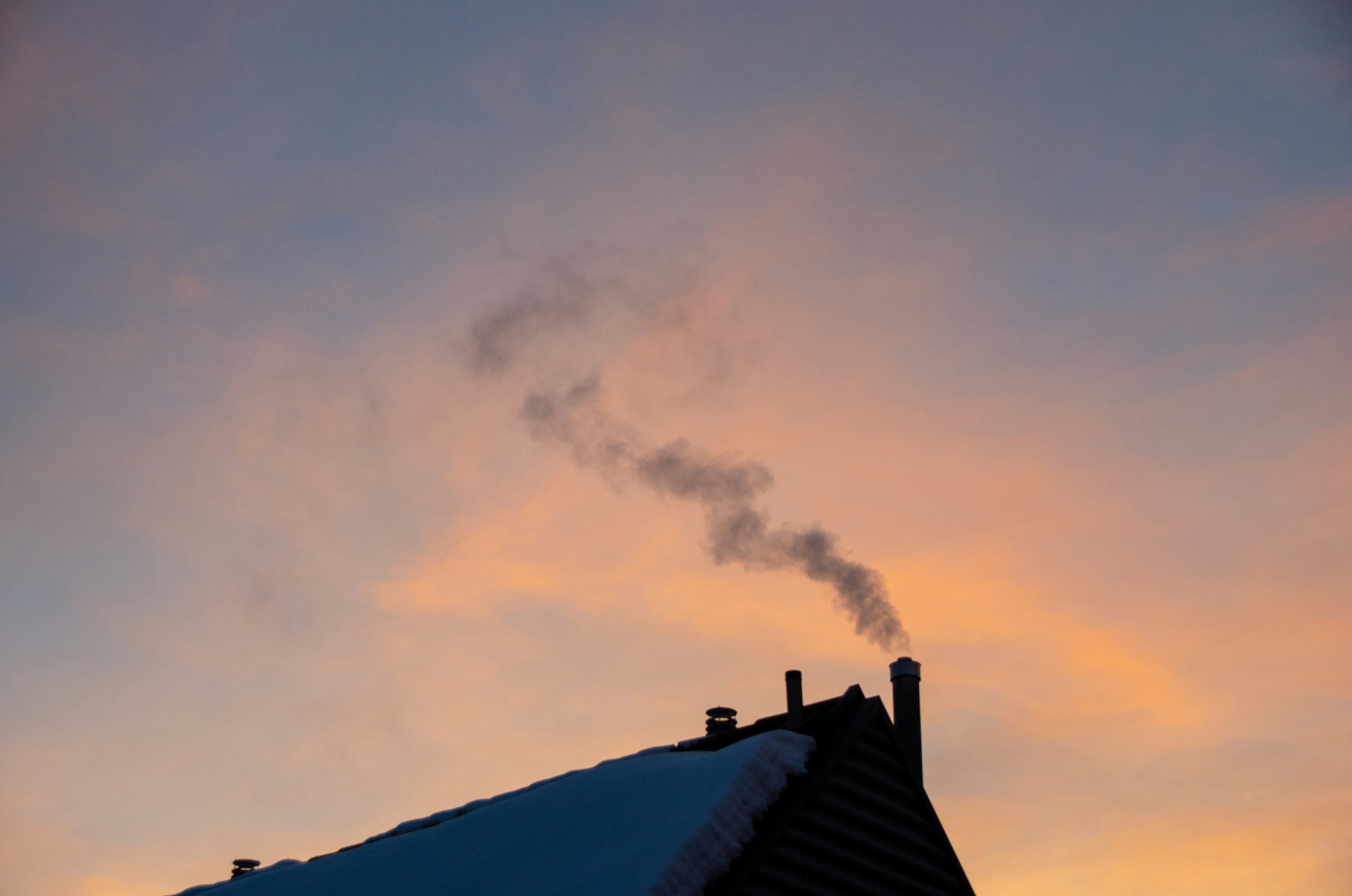 Smoke coming out of the chimney of a house with snowy roof