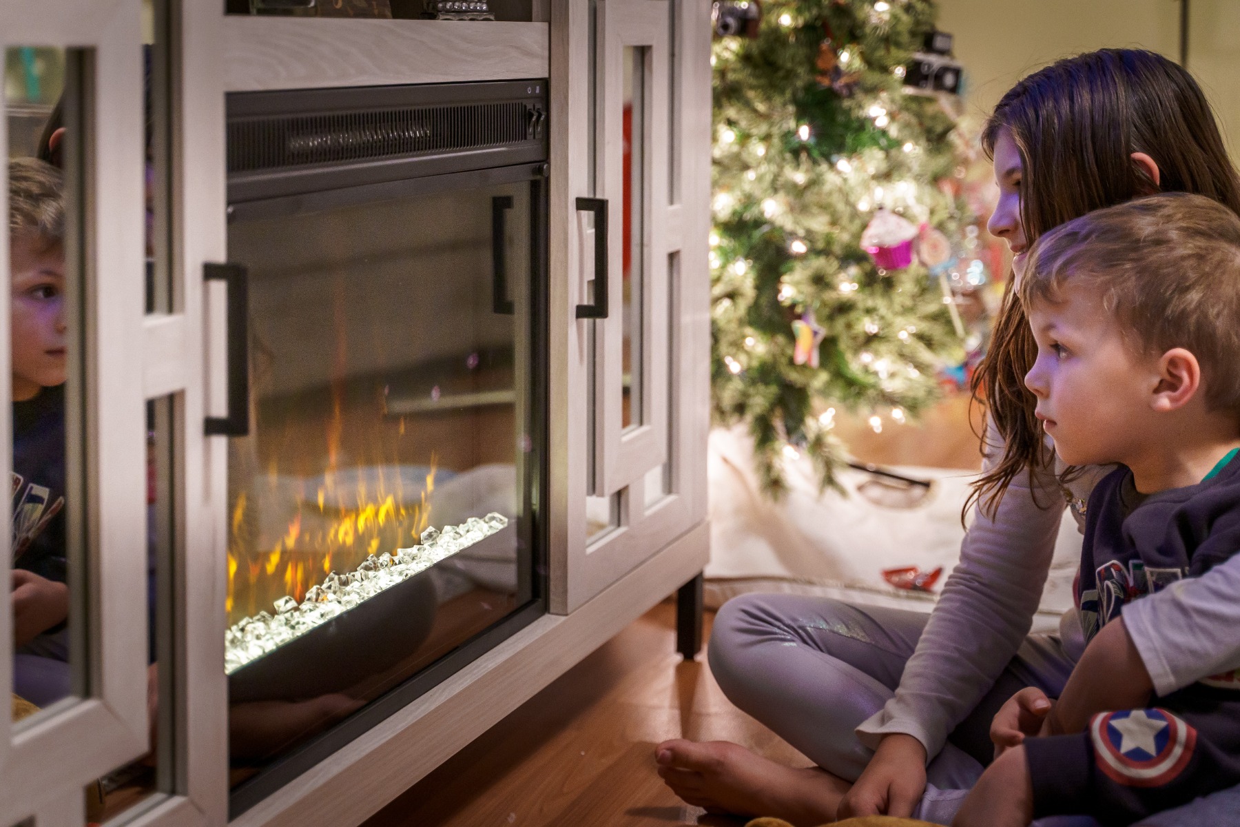 Kids sitting by an electric fireplace