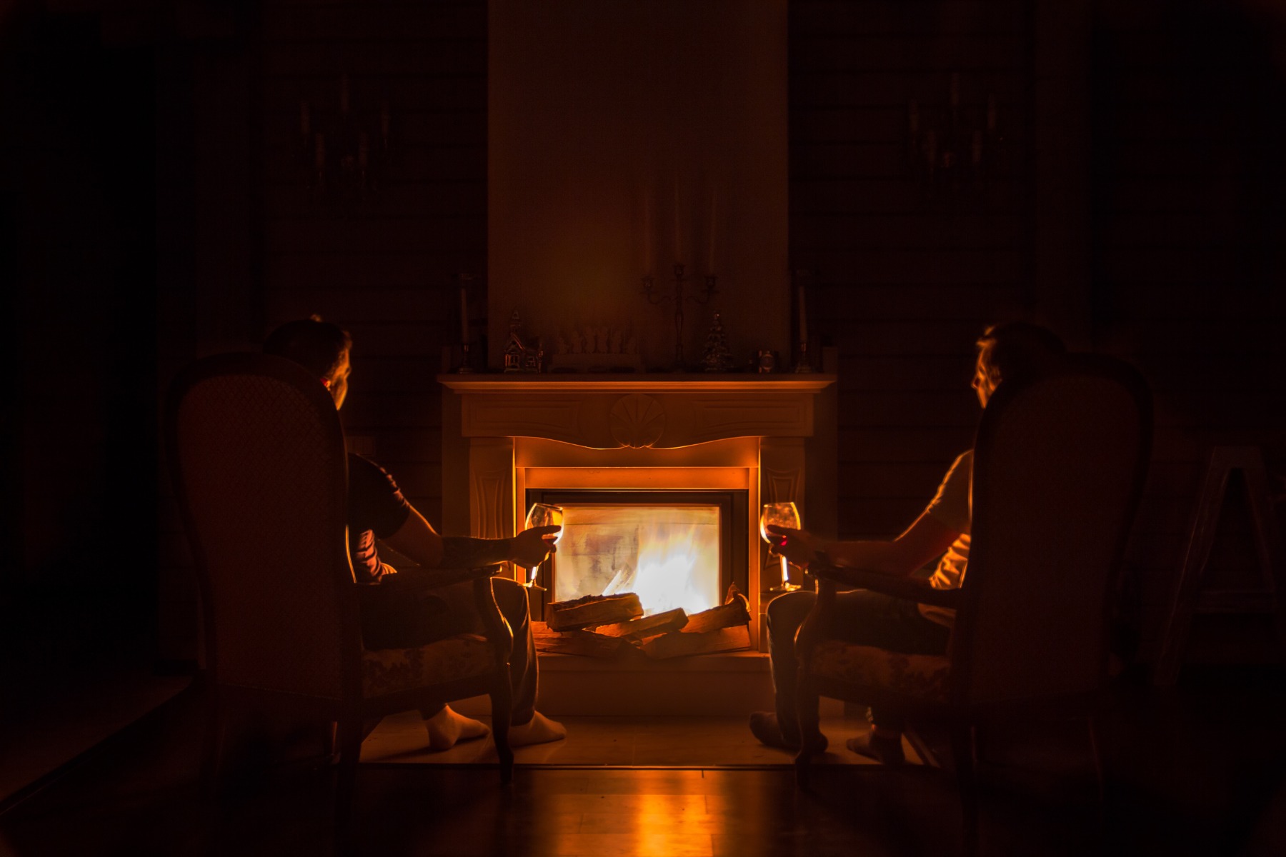 Two people sitting in front of a fireplace with glasses of wine